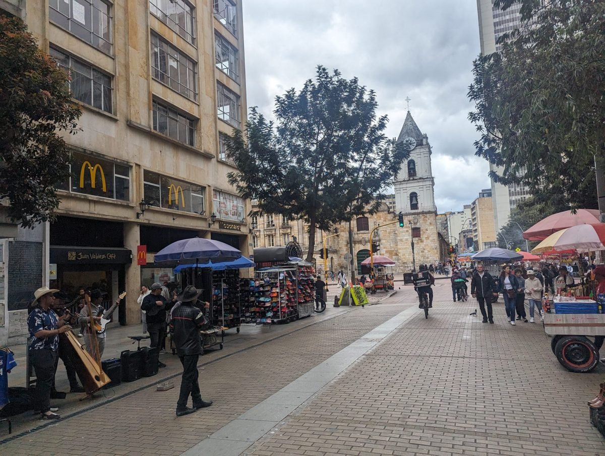 Deptak w centrum Bogoty – uliczni muzykanci z harfą, stragany i biała wieża kościoła w tle