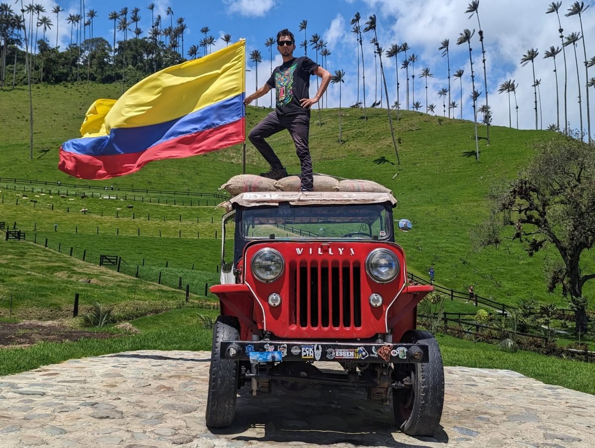 Maciek z flagą Kolumbii na dachu czerwonego jeepa Willys w Valle de Cocora, w tle palmy woskowe