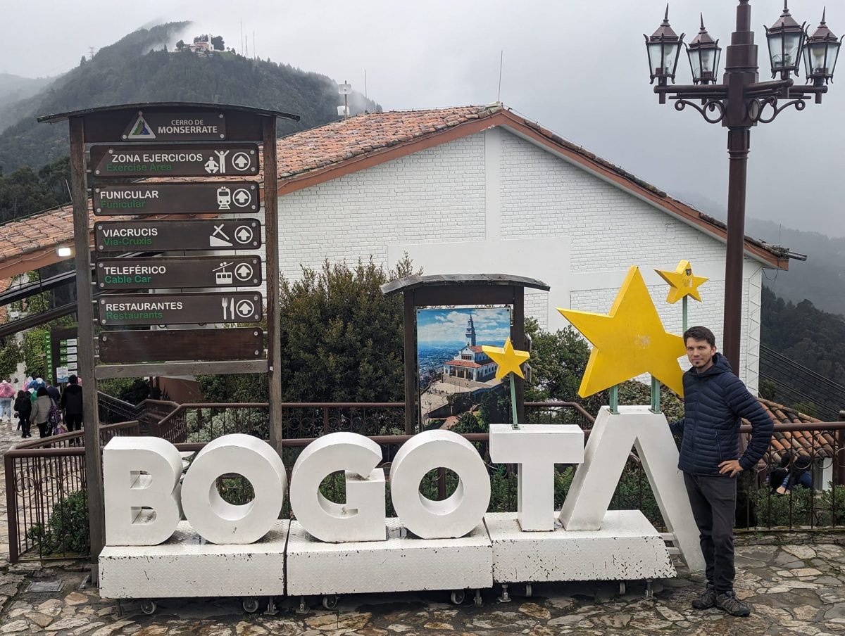 Maciek przy dużym napisie BOGOTA na szczycie Monserrate, obok drogowskaz do kolejek
