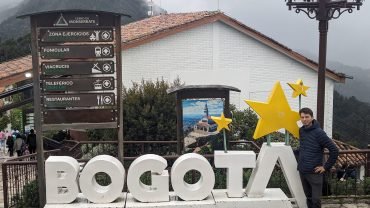 Maciek przy dużym napisie BOGOTA na szczycie Monserrate, obok drogowskaz do kolejek