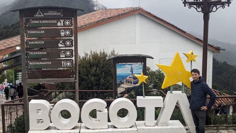 Maciek przy dużym napisie BOGOTA na szczycie Monserrate, obok drogowskaz do kolejek