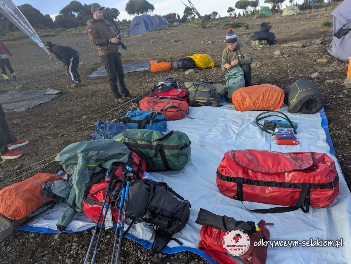 Pakowanie głównych toreb i plecaków na plandece rano w Shira Cave Camp