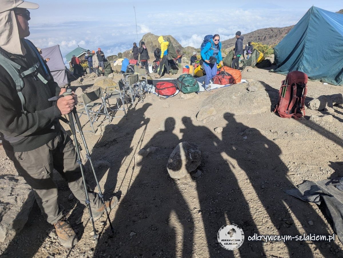 Cienie uczestników z kijami trekkingowymi w porannym słońcu w Karanga Camp
