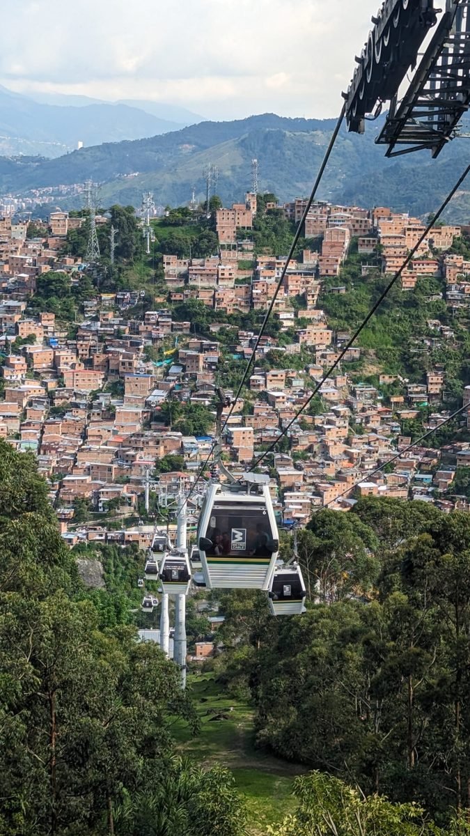 Wagoniki kolejki Metrocable nad lasem i zboczem zabudowanym ceglanymi domami w Medellín