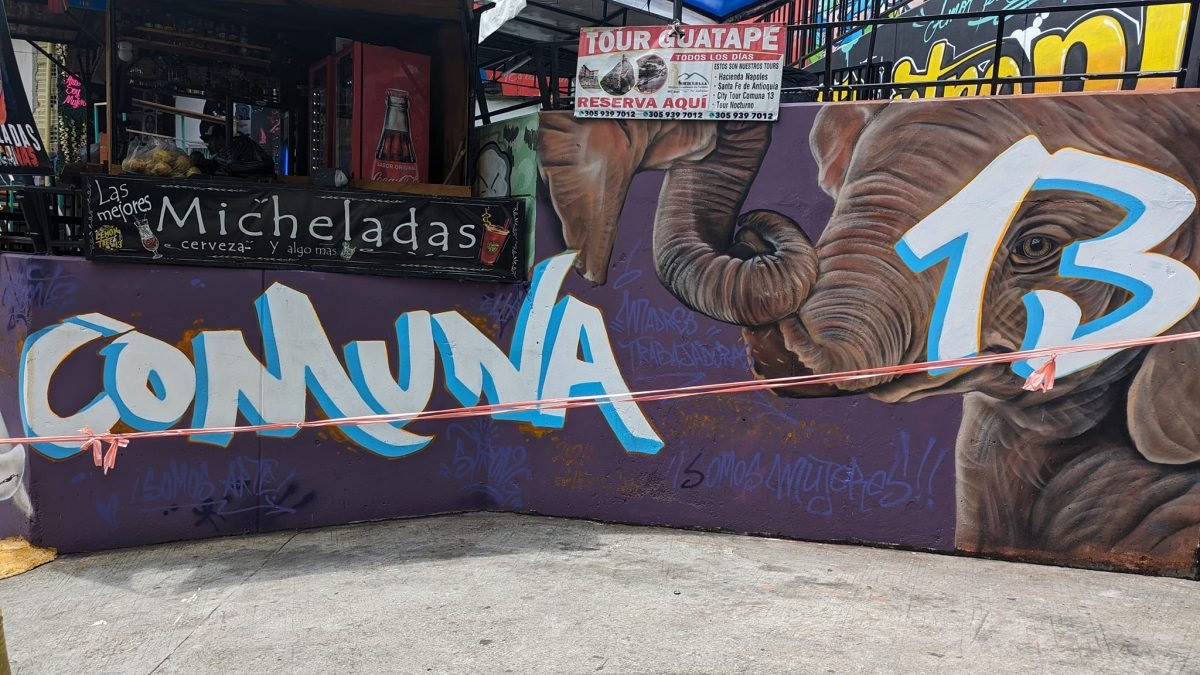 Mural Comuna 13 ze słoniem, nad nim tablica biura z wycieczkami do Guatapé