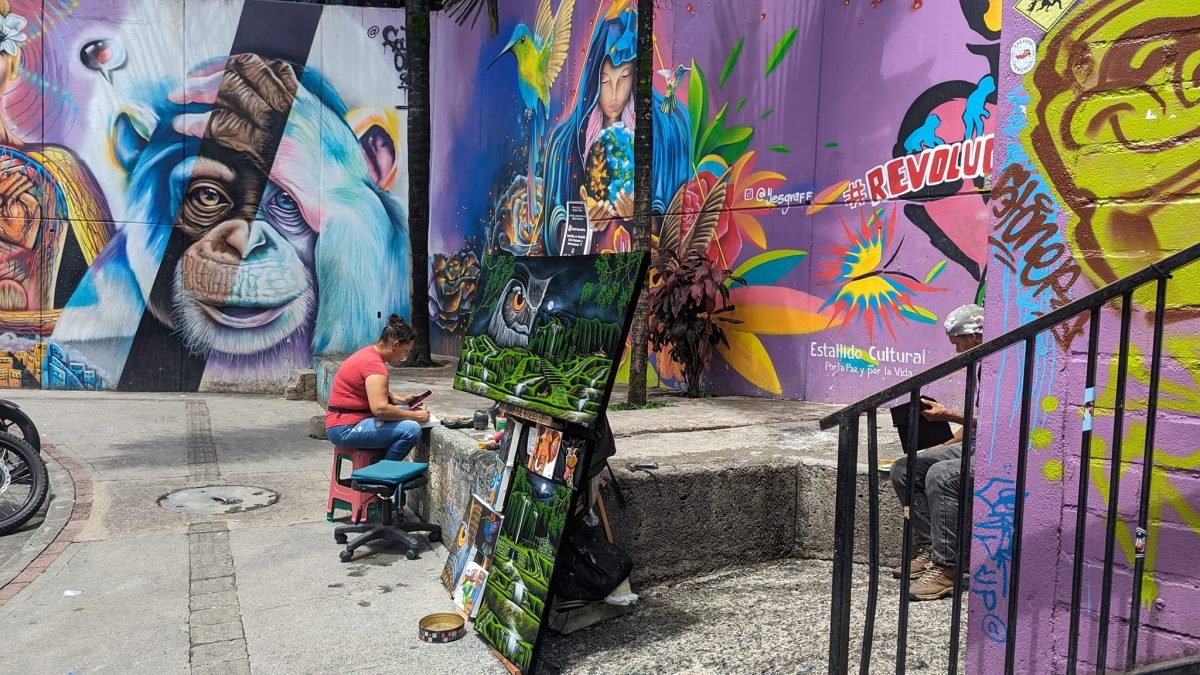 Murale z szympansem i kobietą z kolibrami w Comuna 13, przed nimi malarka sprzedająca obrazy