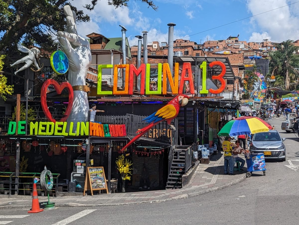 Kolorowy napis Comuna 13 – De Medellín para el mundo i rzeźba papugi nad lokalem w Comuna 13