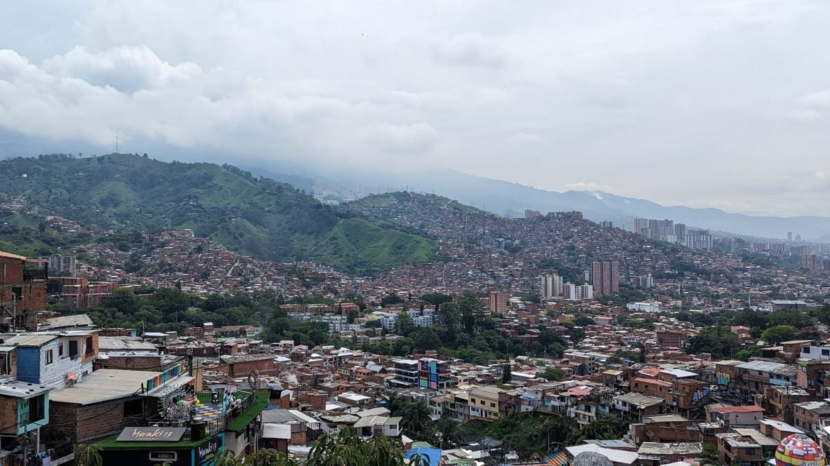Panorama Medellín z Comuna 13 – dzielnice na zielonych wzgórzach i wieżowce w dolinie pod chmurami