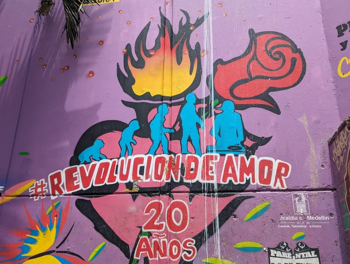 Mural z płonącym sercem i napisem Revolución de amor 20 años na fioletowej ścianie w Comuna 13
