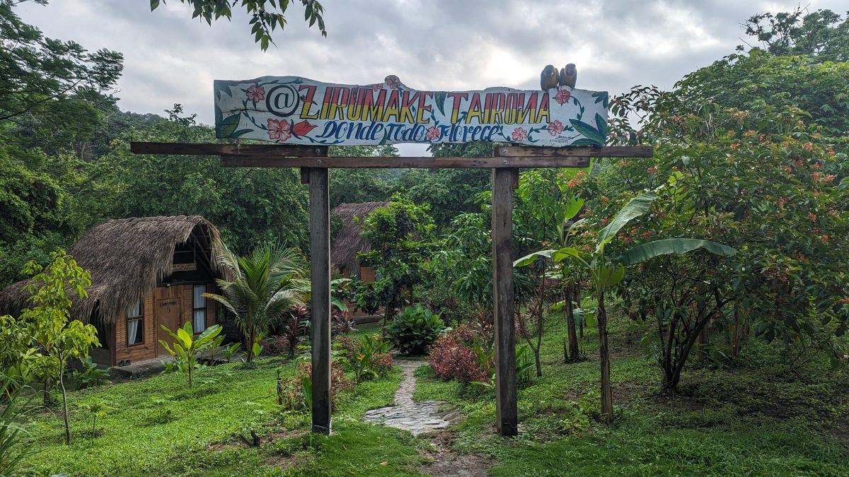 Brama z szyldem Zirumake Tairona i domki pod strzechą wśród tropikalnej zieleni