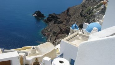 Białe domy Oia nad kalderą Santorini z niebieską kopułą kościoła