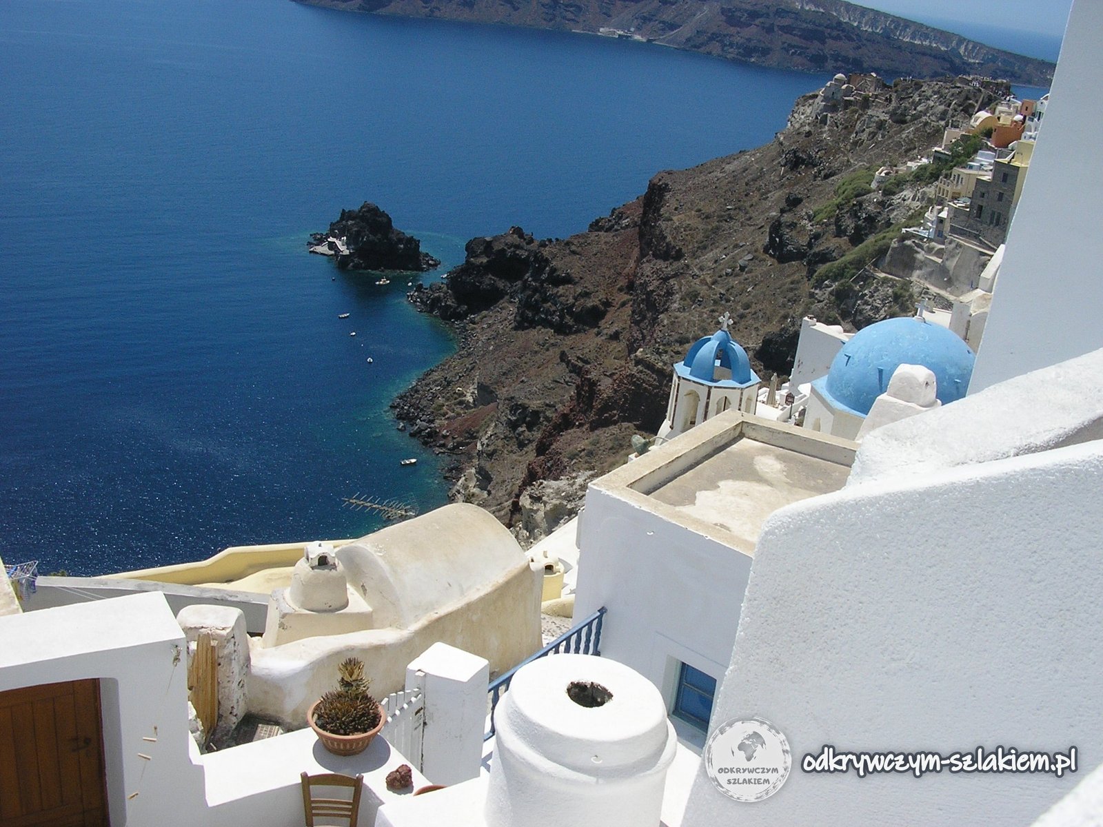 Białe domy Oia nad kalderą Santorini z niebieską kopułą kościoła
