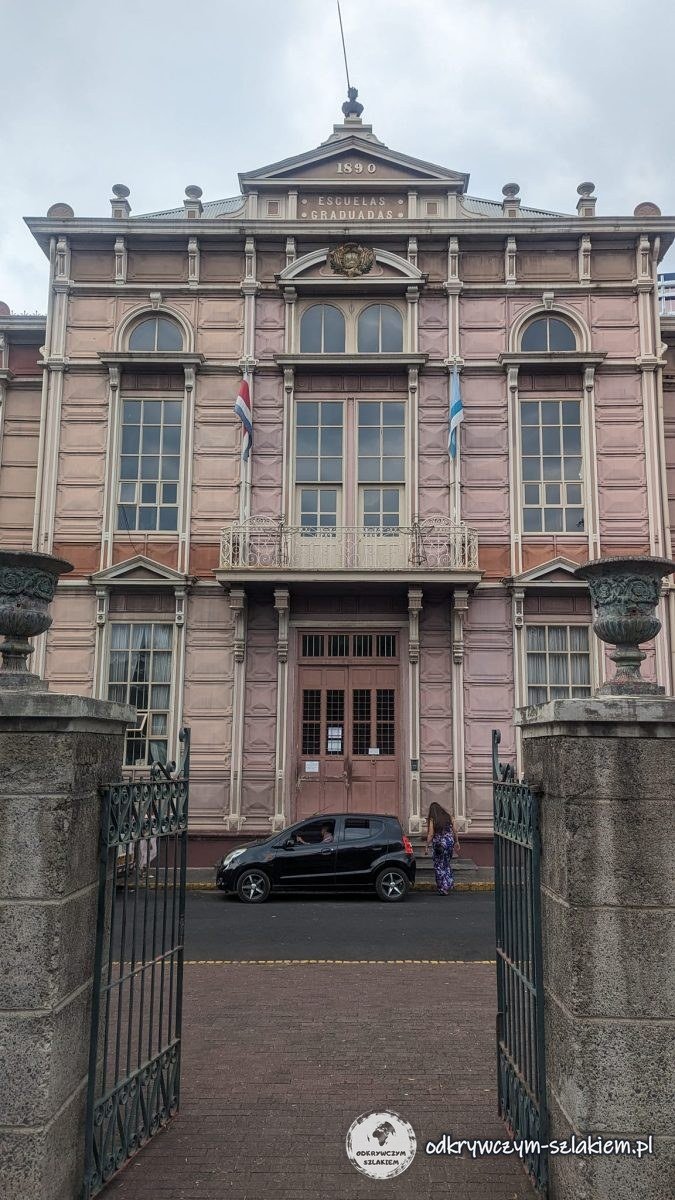 Różowy zabytkowy gmach z flagami za żelazną bramą w San José
