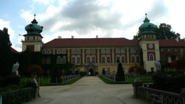 Aleja z cisami przyciętymi w stożki prowadząca do bramy zamku w Łańcucie, z dwiema wieżami o zielonych hełmach