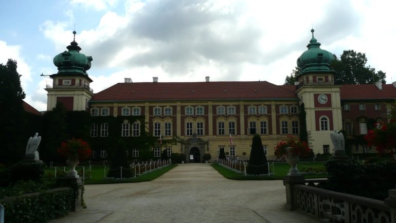 Aleja z cisami przyciętymi w stożki prowadząca do bramy zamku w Łańcucie, z dwiema wieżami o zielonych hełmach