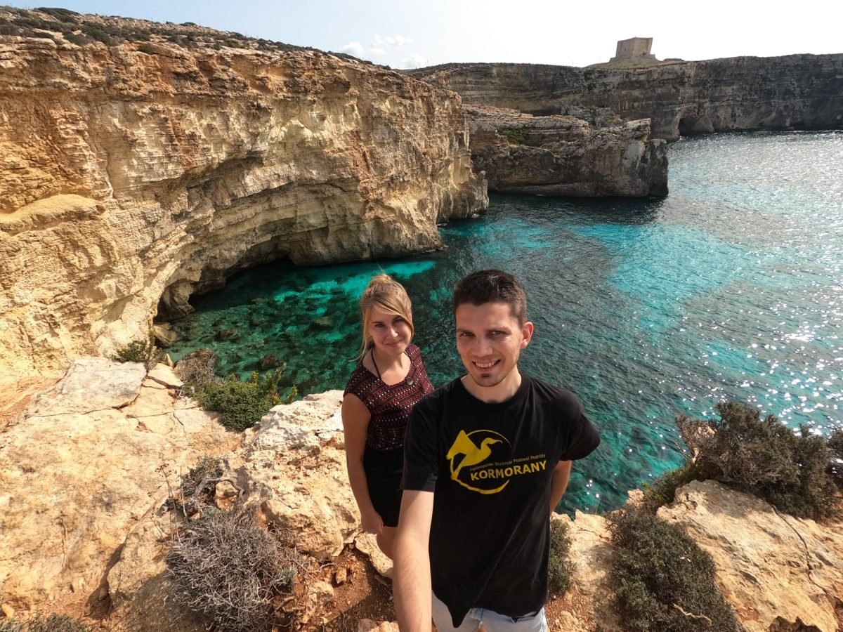 Patrycja i Maciek na klifie nad Crystal Lagoon na Comino, w tle wieża św. Marii
