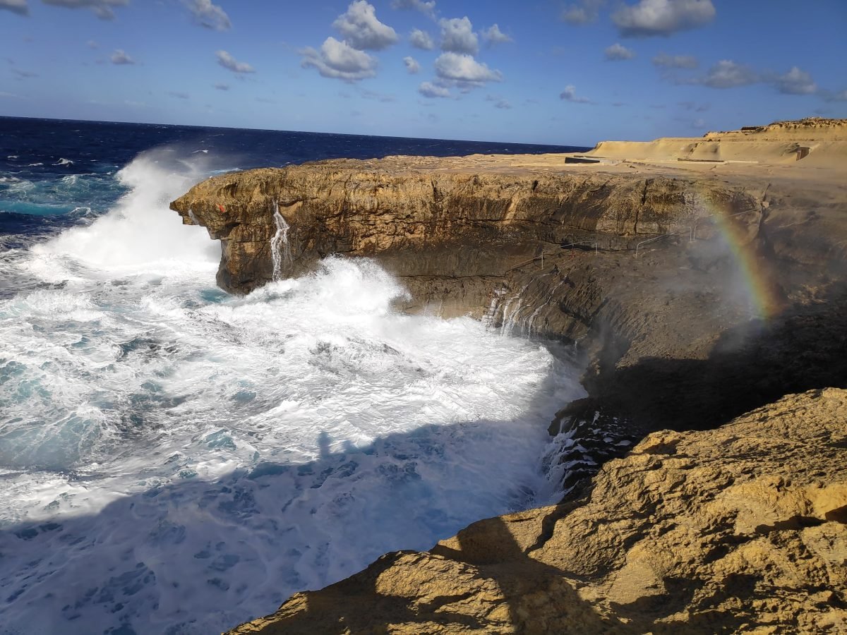 Fale przy klifach obok solnisk na Gozo, po prawej tęcza