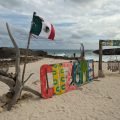 Kolorowy napis „Cozumel” i meksykańskie flagi na plaży na wschodnim wybrzeżu wyspy