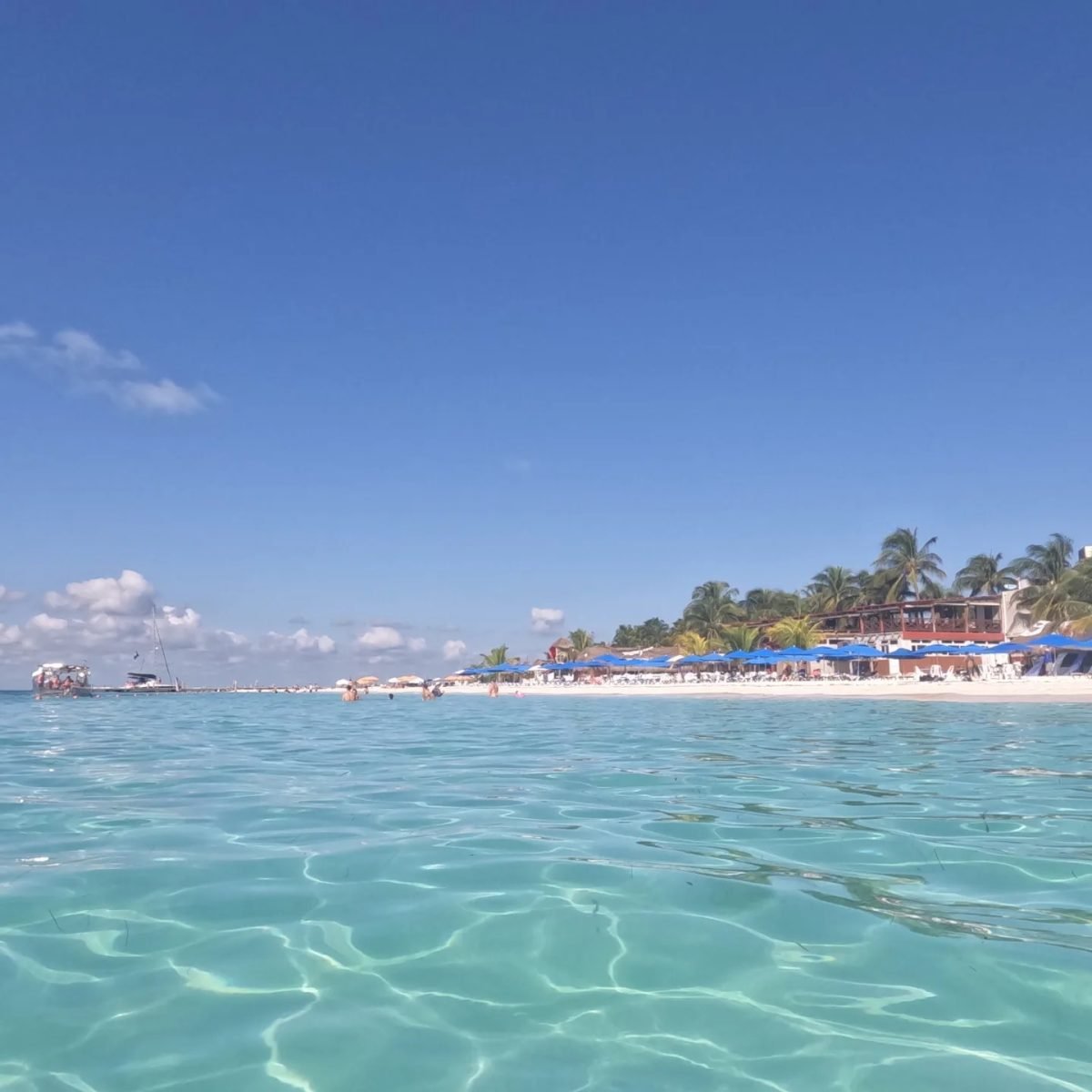 Turkusowa woda przy plaży Playa Norte na Isla Mujeres, w tle leżaki i łodzie