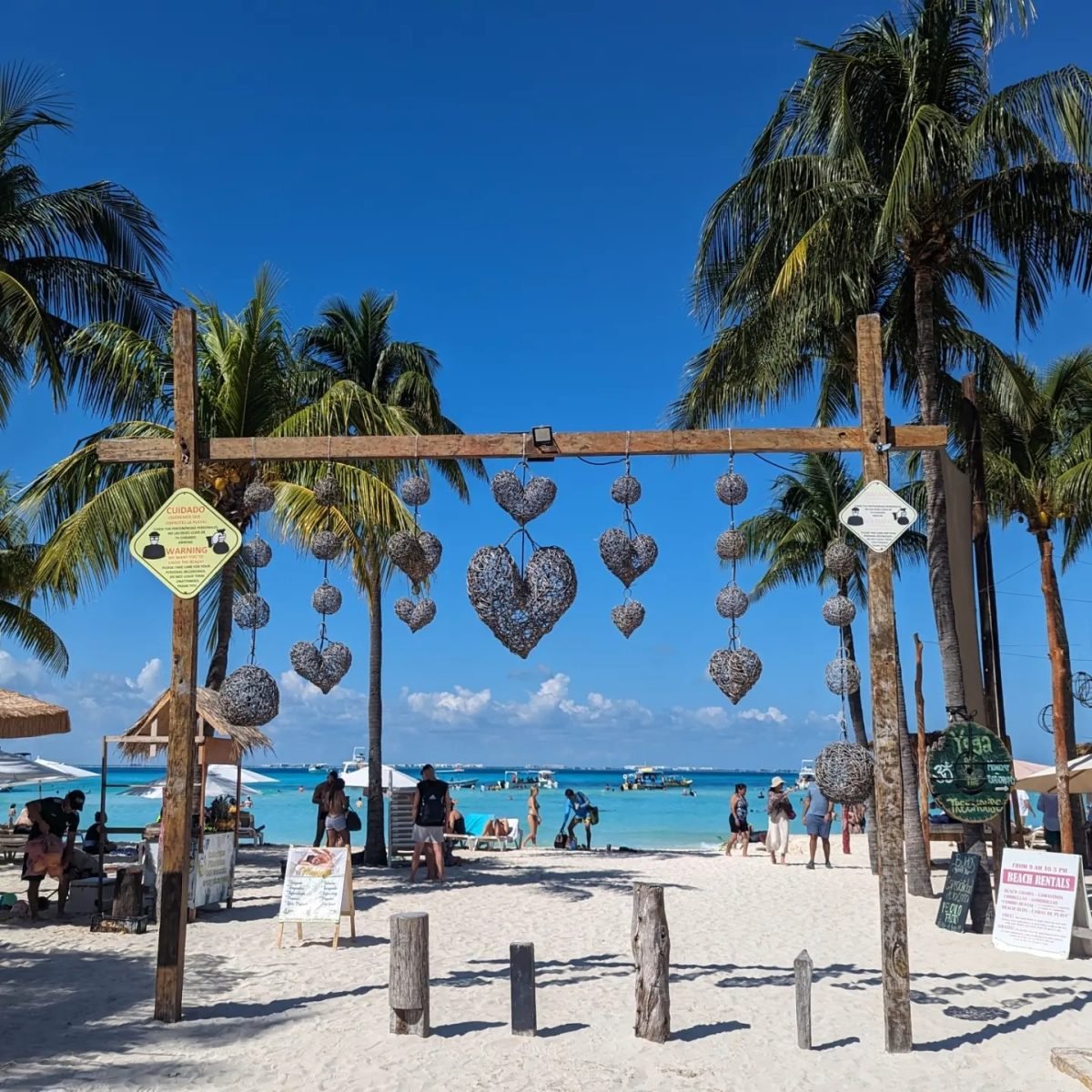 Drewniana brama z zawieszonymi sercami na plaży Playa Norte na Isla Mujeres, w tle turkusowe morze