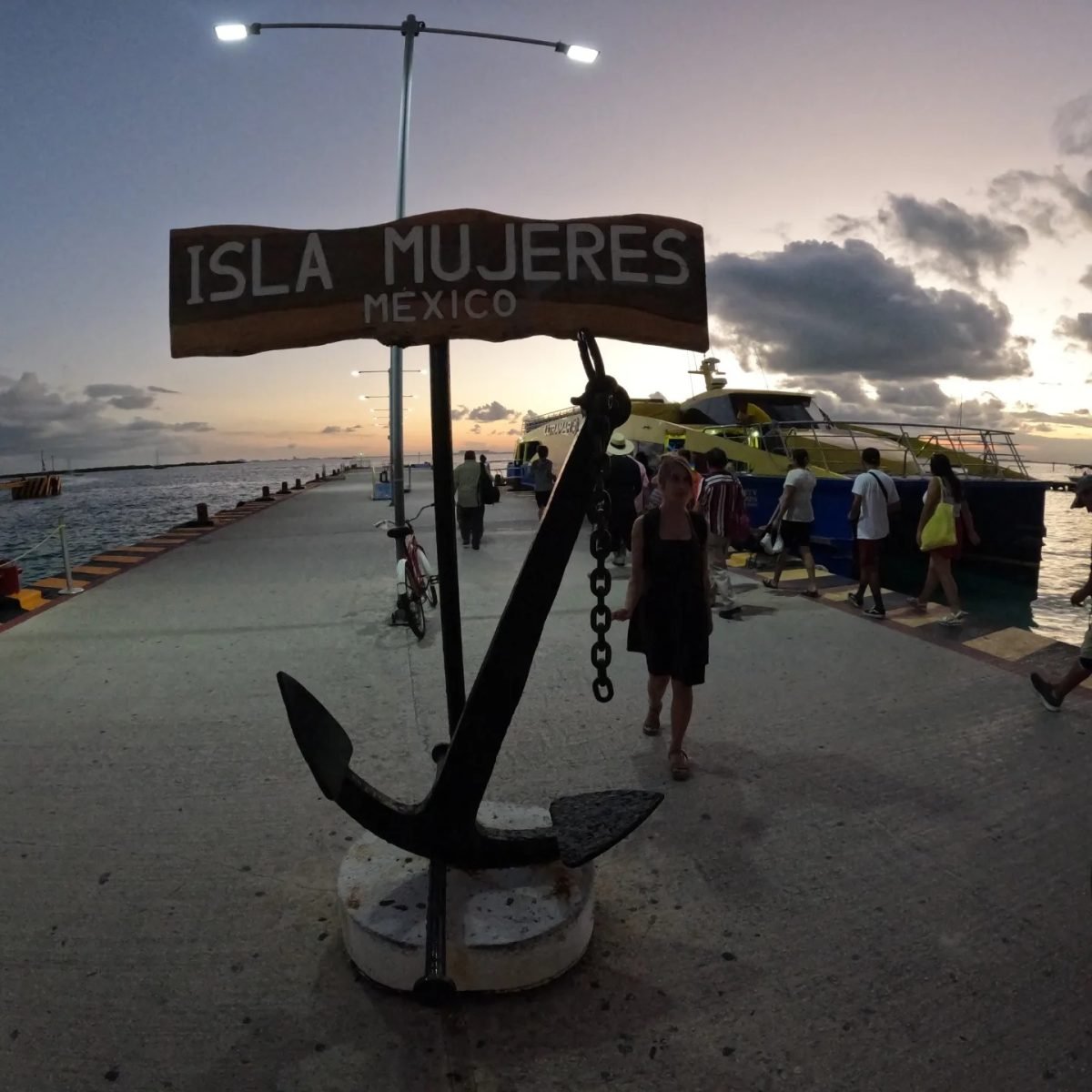 Napis „Isla Mujeres” i kotwica na nabrzeżu przy przystani promowej o zachodzie słońca