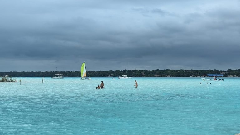 Turkusowa woda laguny Bacalar z żaglówką i pływającymi ludźmi
