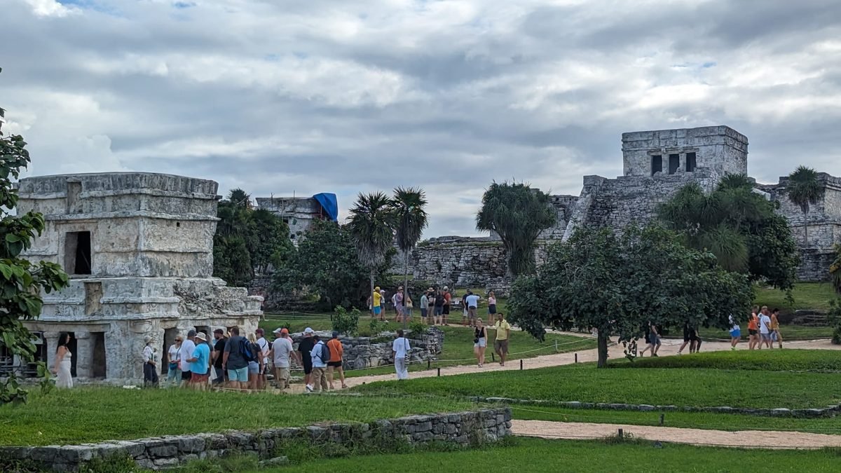 Kamienne świątynie w ruinach Tulum i zwiedzający na trawiastych alejkach