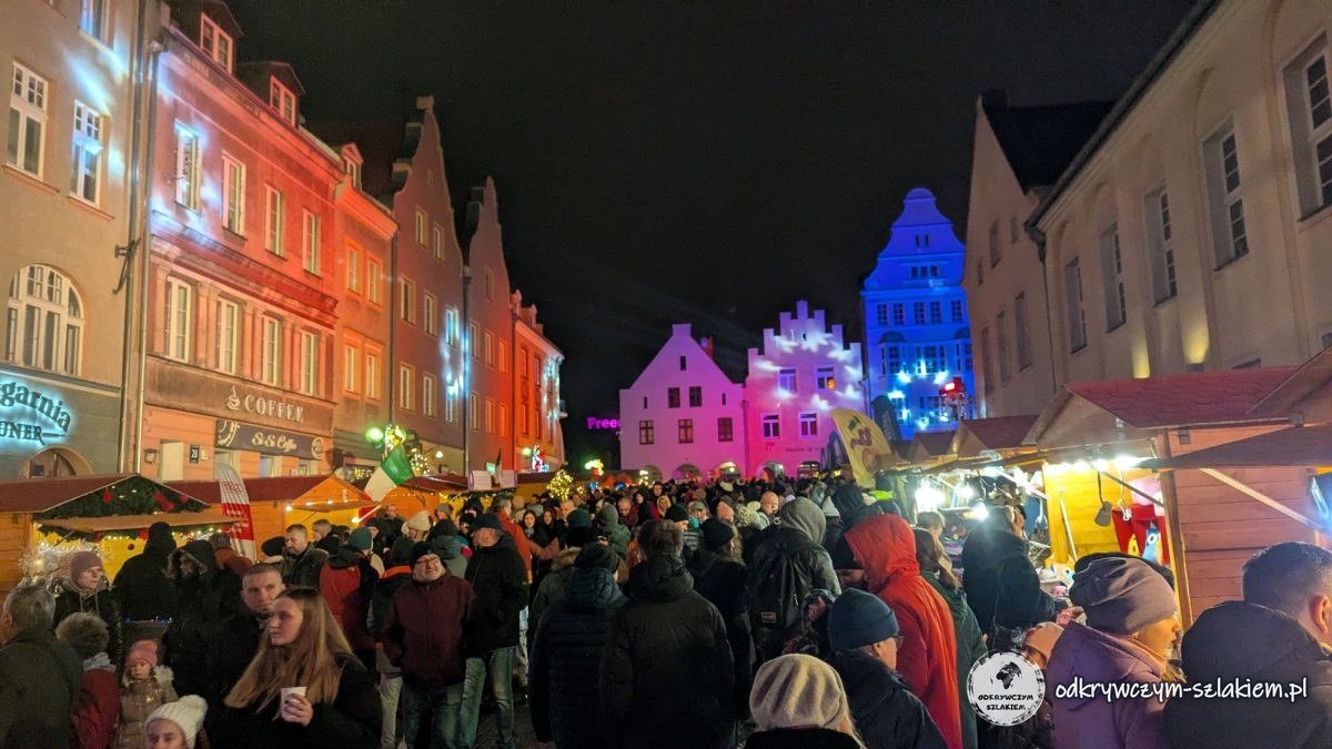 Crowds at the Christmas market on Olsztyn's Market Square, with town houses lit in pink and blue