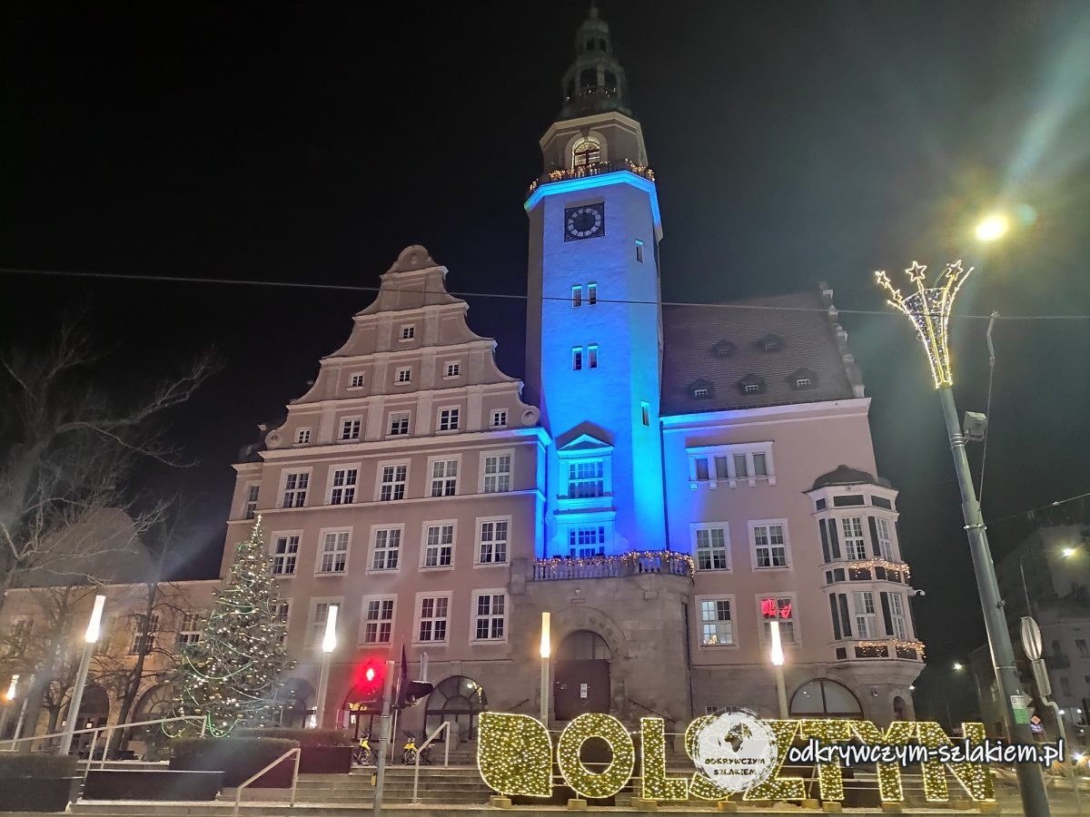 Olsztyn's New Town Hall with its tower lit in blue and an illuminated OLSZTYN sign in December