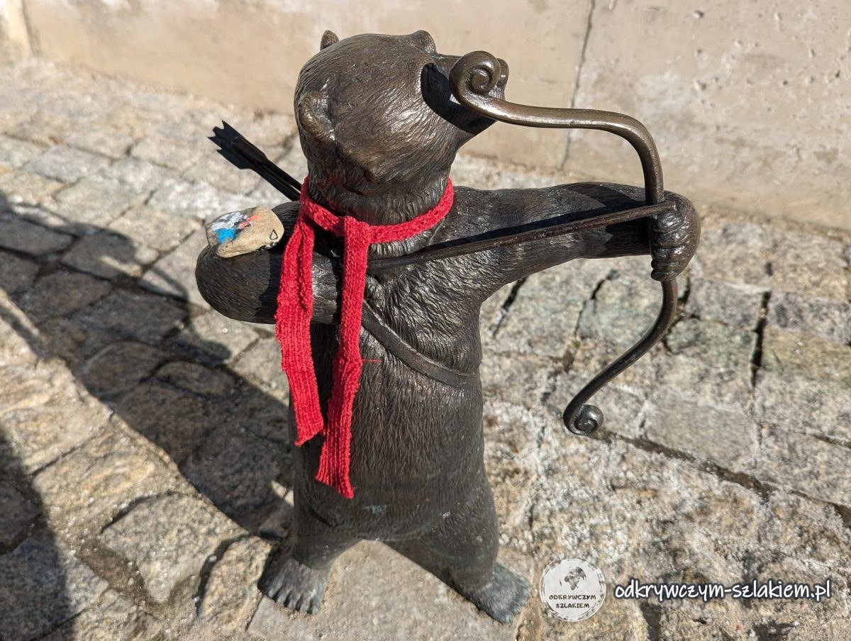 Bärenfigur als Bogenschütze mit rotem Schal auf dem Gehweg in Białystok