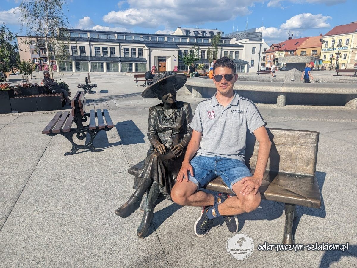 Maciek sitzt auf der Bank neben der Figur von Hanka Bielicka auf dem Alten Markt in Łomża