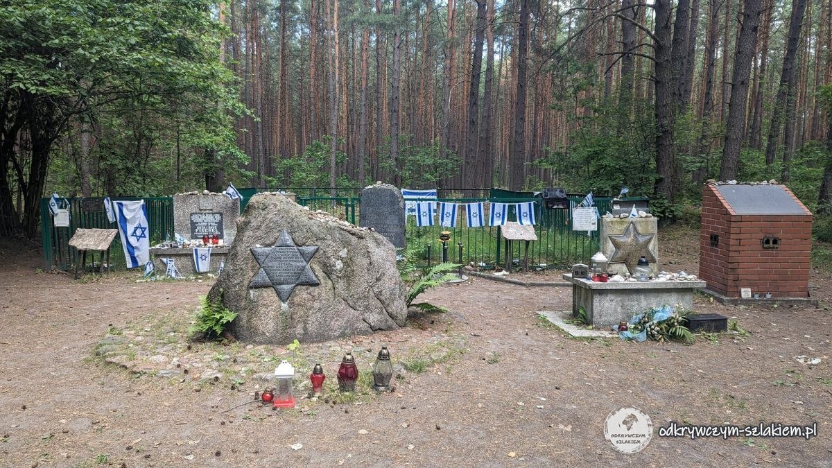 Umzäunte Gedenkstätte im Wald von Łopuchowo mit einem Findling mit Davidstern, Gedenktafeln und israelischen Fahnen