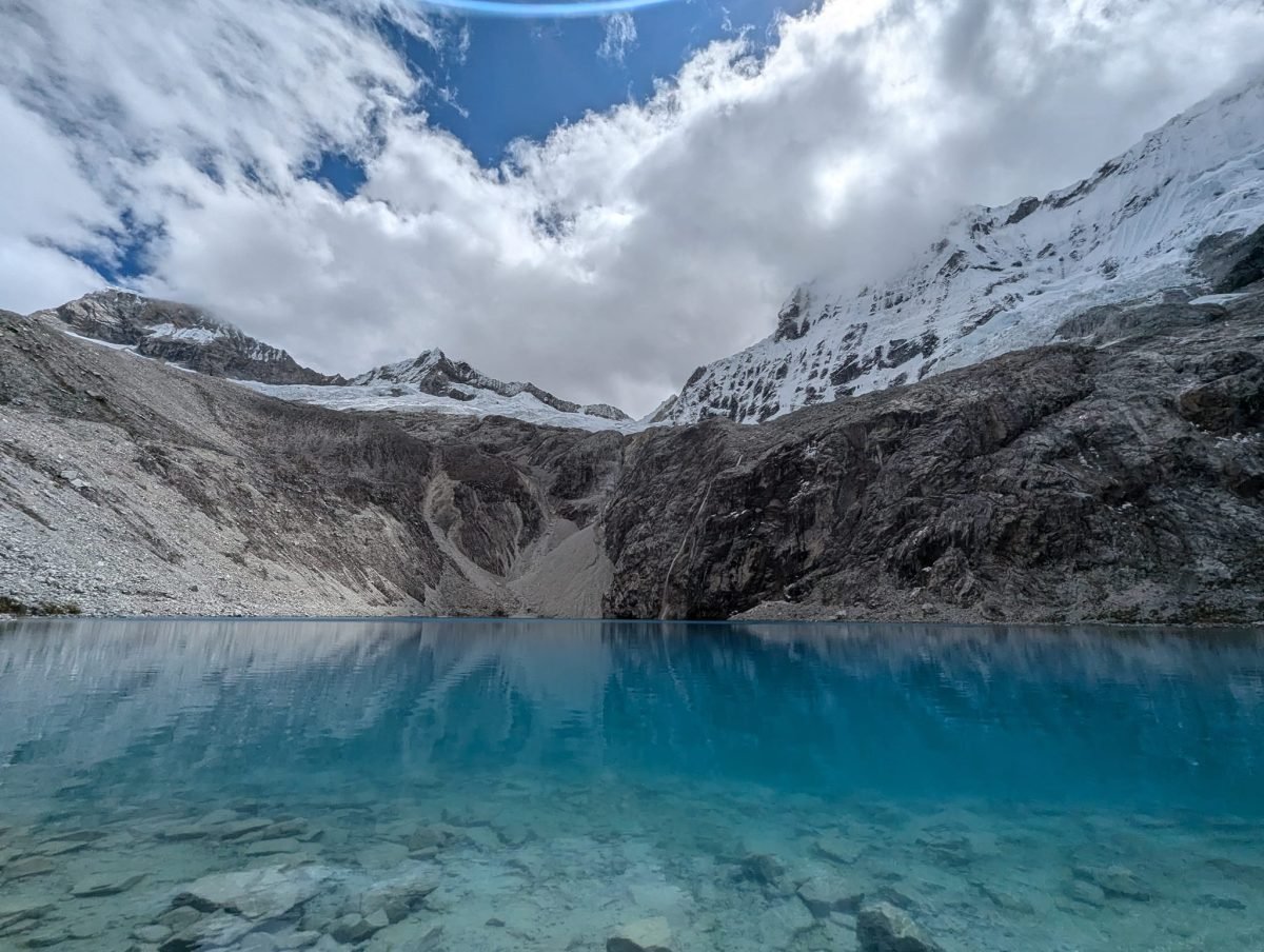 Laguna 69 z brzegu – przejrzysta turkusowa woda, za nią szare skalne ściany i lodowce w chmurach