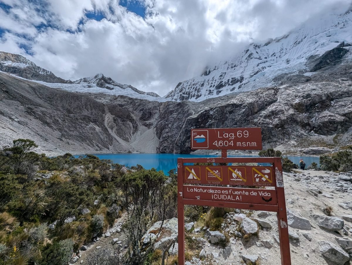 Tabliczka Lag. 69, 4604 m n.p.m. przy szlaku, za nią turkusowa Laguna 69 pod ośnieżonymi zboczami