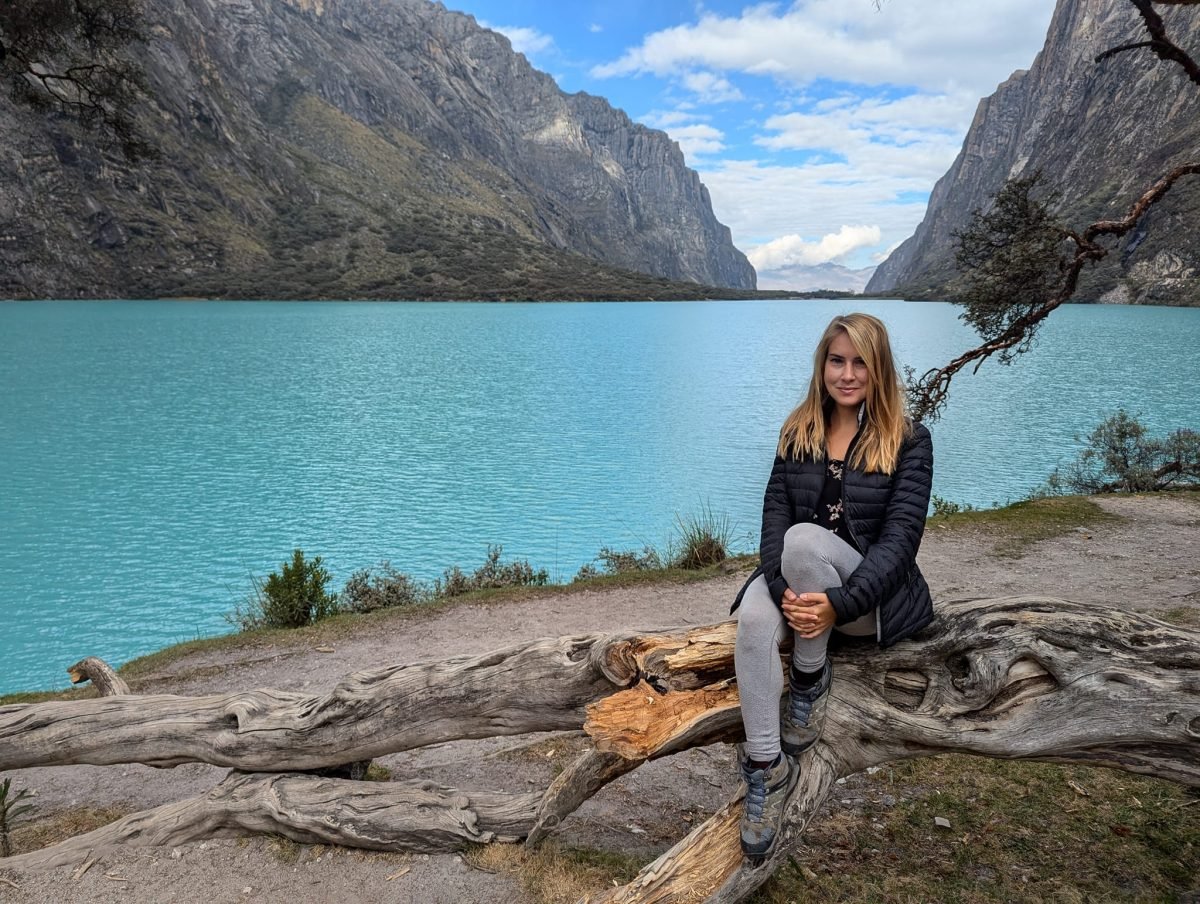 Patrycja siedzi na zwalonym pniu nad turkusową laguną w dolinie Llanganuco, otoczoną stromymi ścianami skalnymi