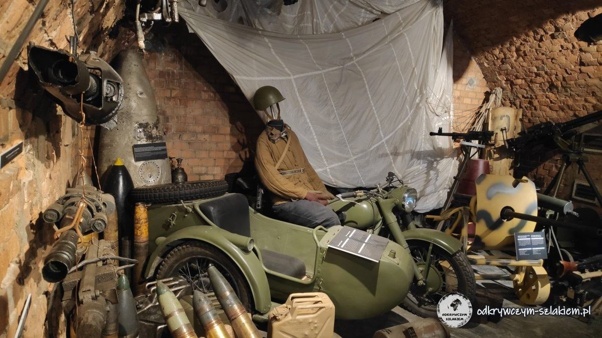 A motorcycle with a sidecar, weapons and a mannequin in uniform in a brick room of the museum at the Citadel