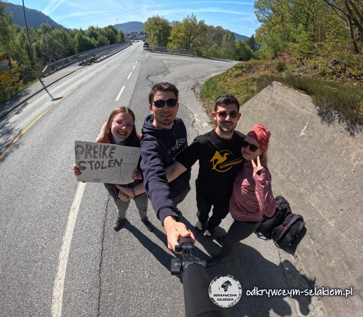 Cuatro personas con un cartel que dice Preikestolen haciendo autostop en la carretera desde Jørpeland