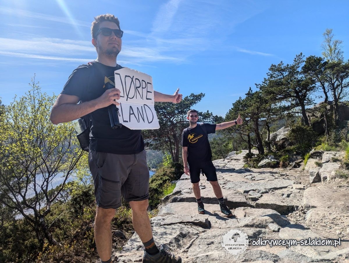 Maciek con un cartel de cartón que dice Jørpeland en el sendero rocoso bajo Preikestolen