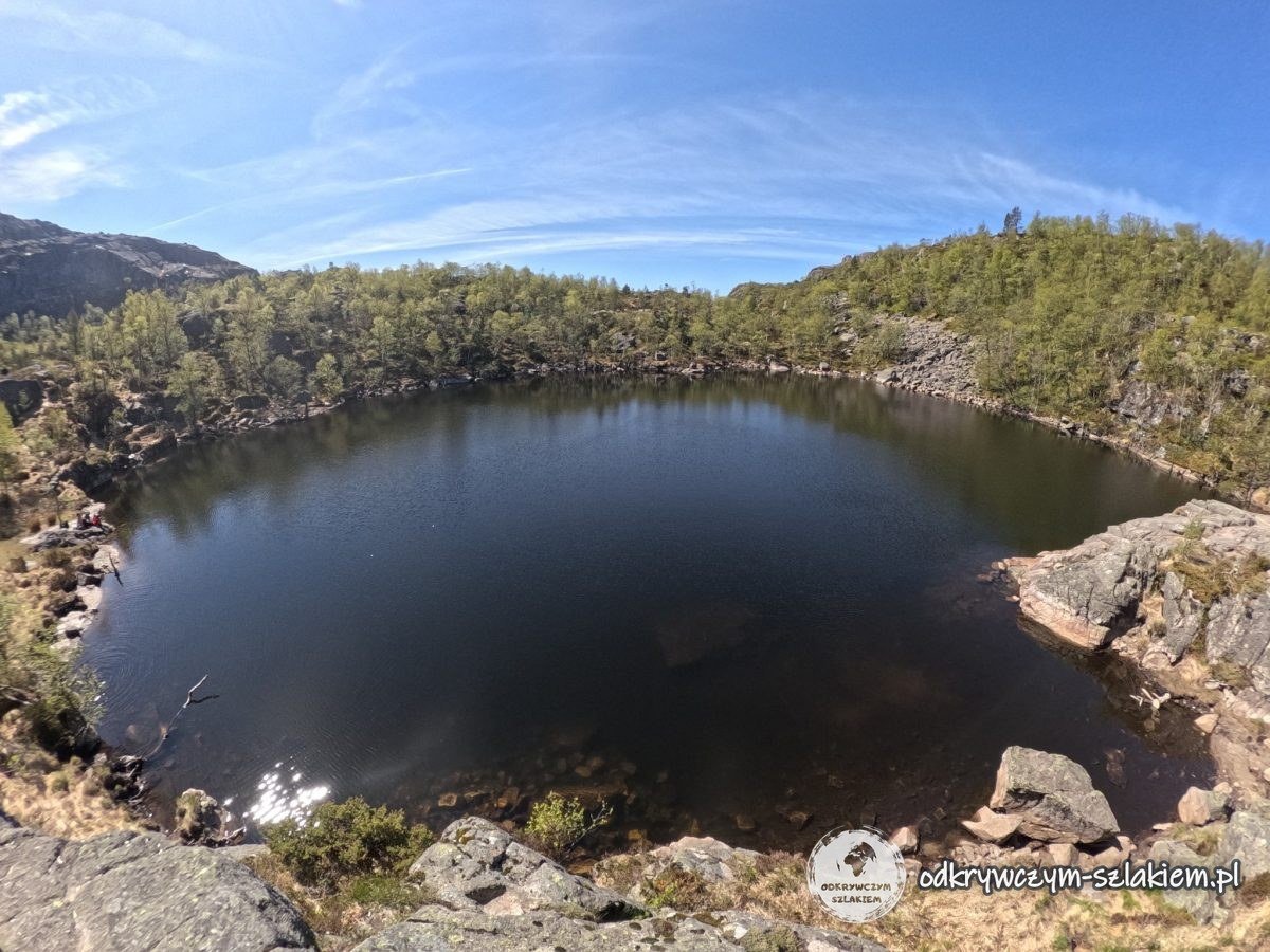 Un pequeño lago oscuro rodeado de rocas y bosque junto al sendero a Preikestolen