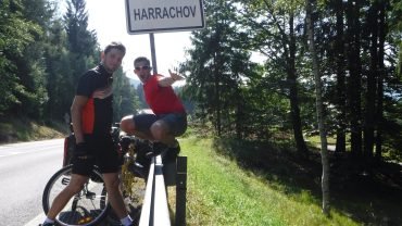 Maciek i Michał z rowerami obładowanymi sakwami przy tablicy miejscowości Harrachov, tuż za granicą polsko-czeską