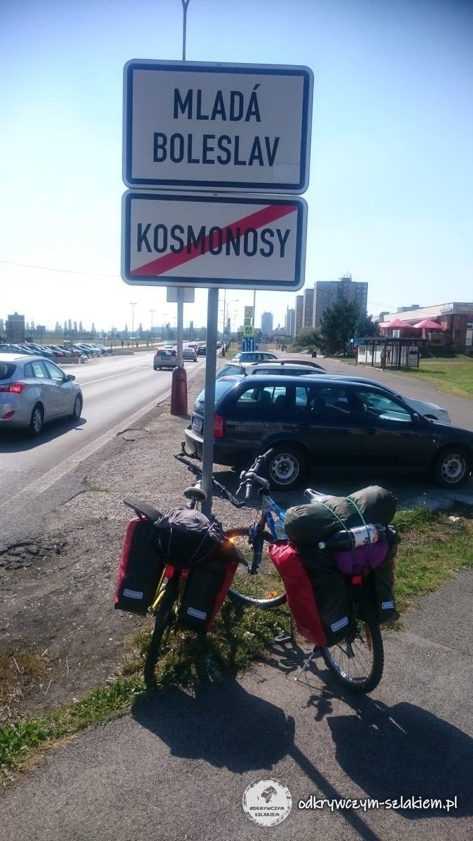 Dos bicis con alforjas bajo el cartel de Mladá Boleslav y el cartel tachado de Kosmonosy junto a la carretera
