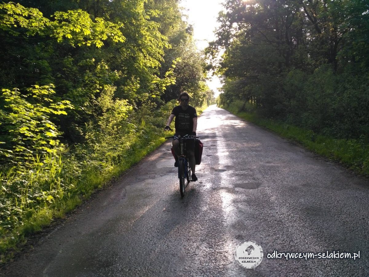 Rowerzysta z sakwami jedzie mokrą drogą w świetle zachodzącego słońca