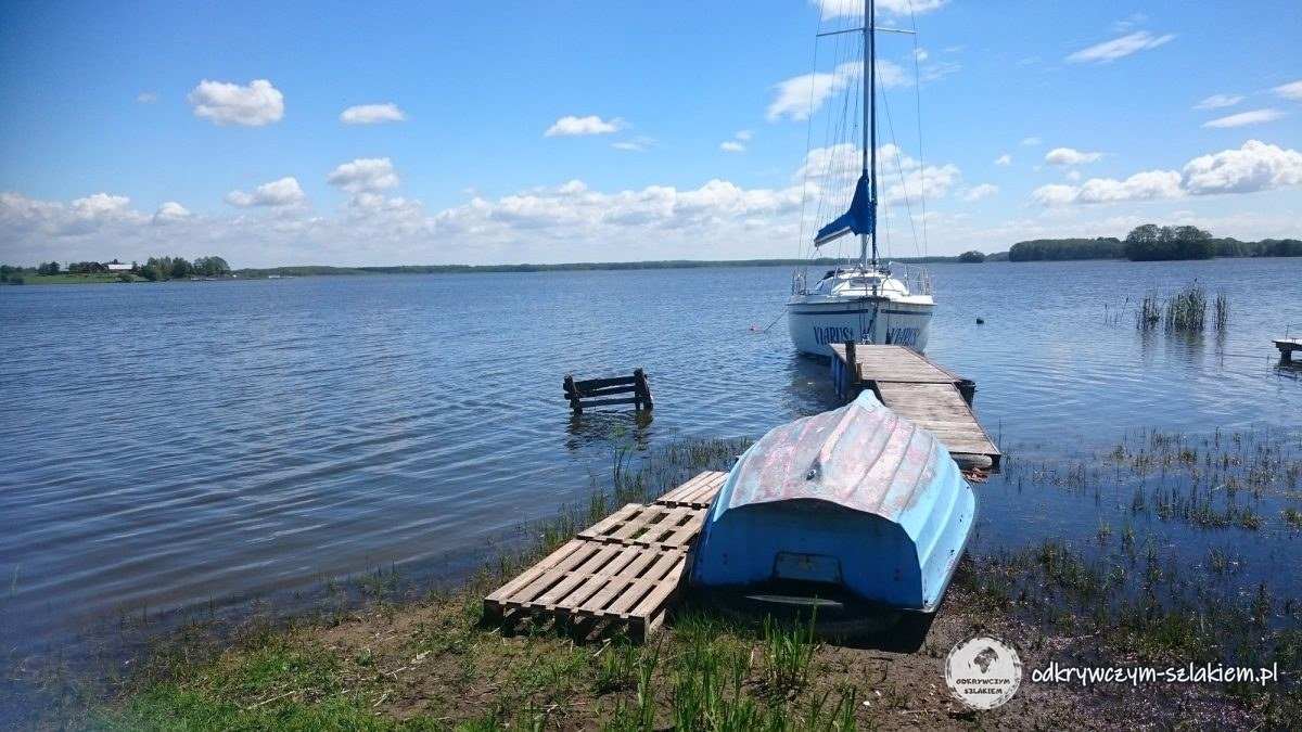 Jezioro z drewnianym pomostem, łódką i jachtem przy brzegu w słoneczny dzień