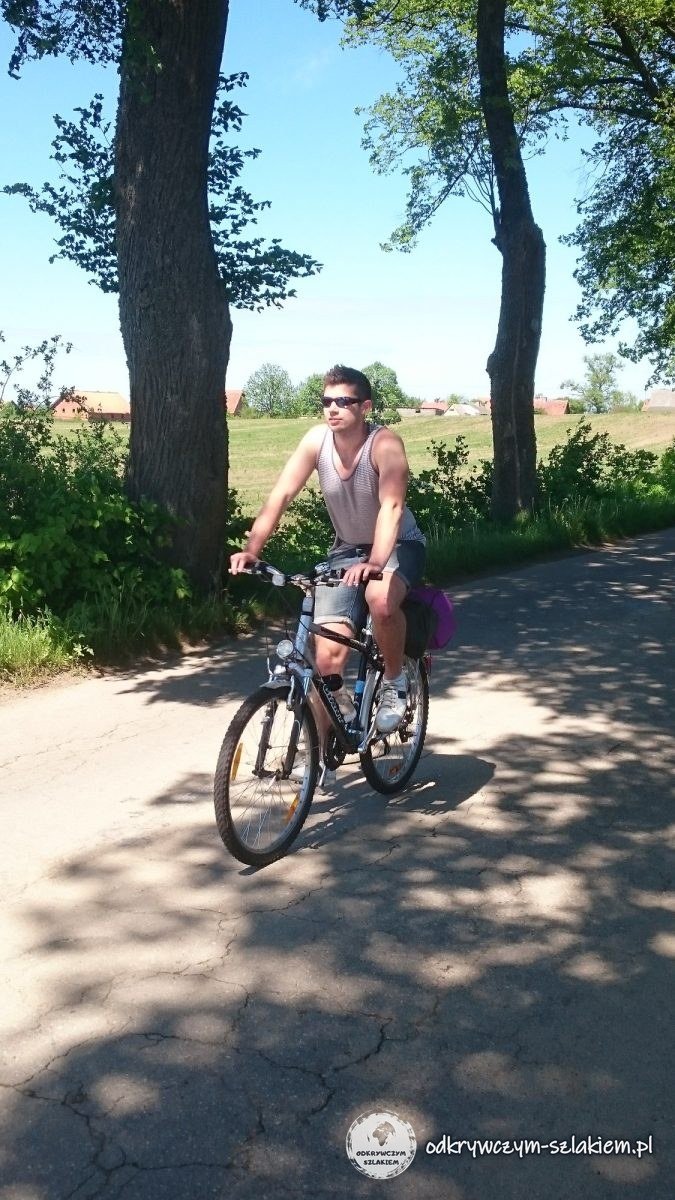 Michał jedzie rowerem drogą obsadzoną drzewami w okolicy Dobrzyk