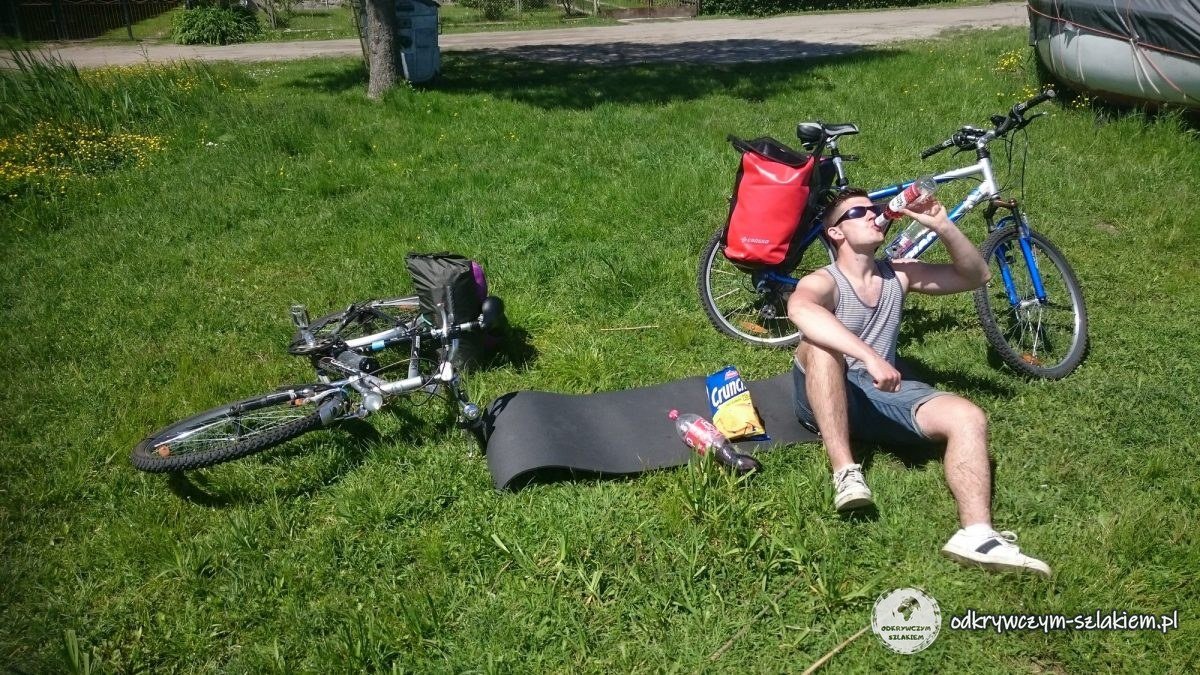 Michał odpoczywa na trawie nad jeziorem obok rowerów i karimaty