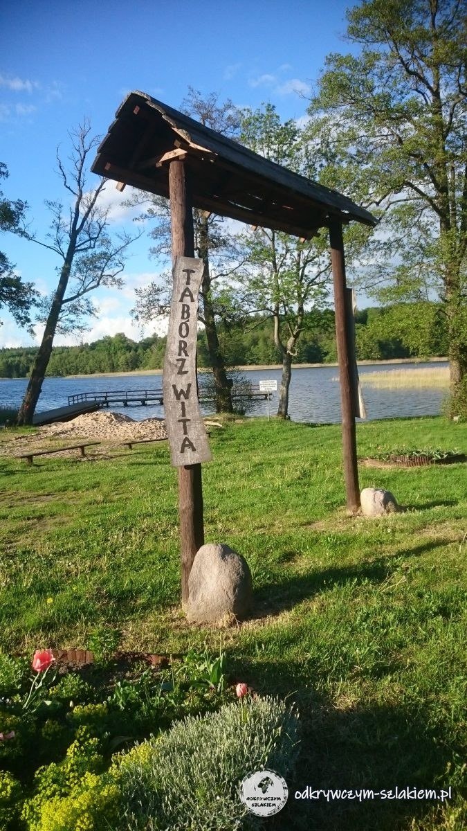 Drewniany witacz wsi Tabórz na trawniku nad jeziorem