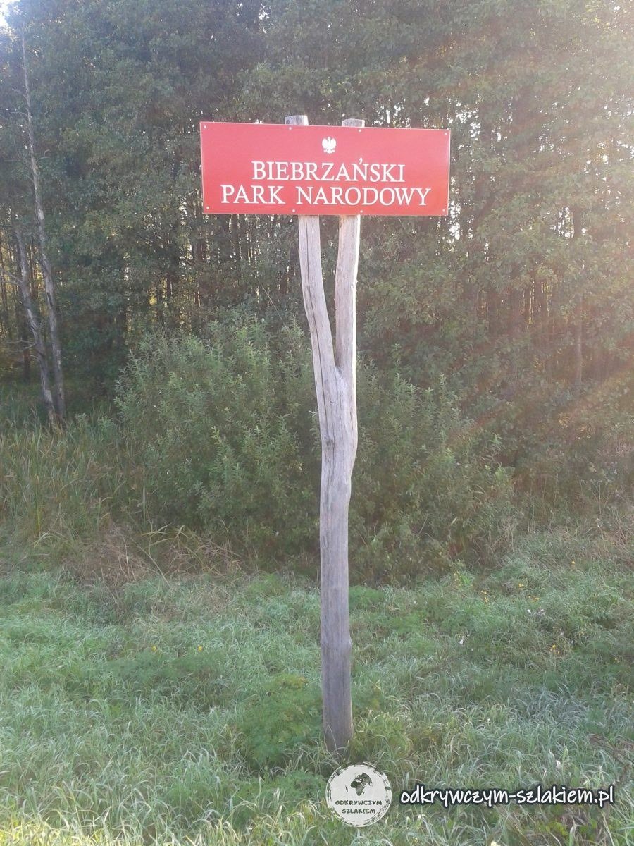 Rotes Schild des Biebrza-Nationalparks an einem Holzpfosten zwischen Sträuchern