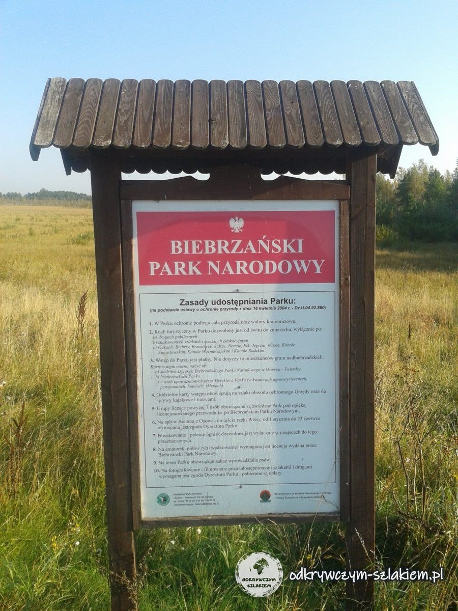 Tafel mit den Besucherregeln des Biebrza-Nationalparks unter einem Holzdach auf einer Wiese