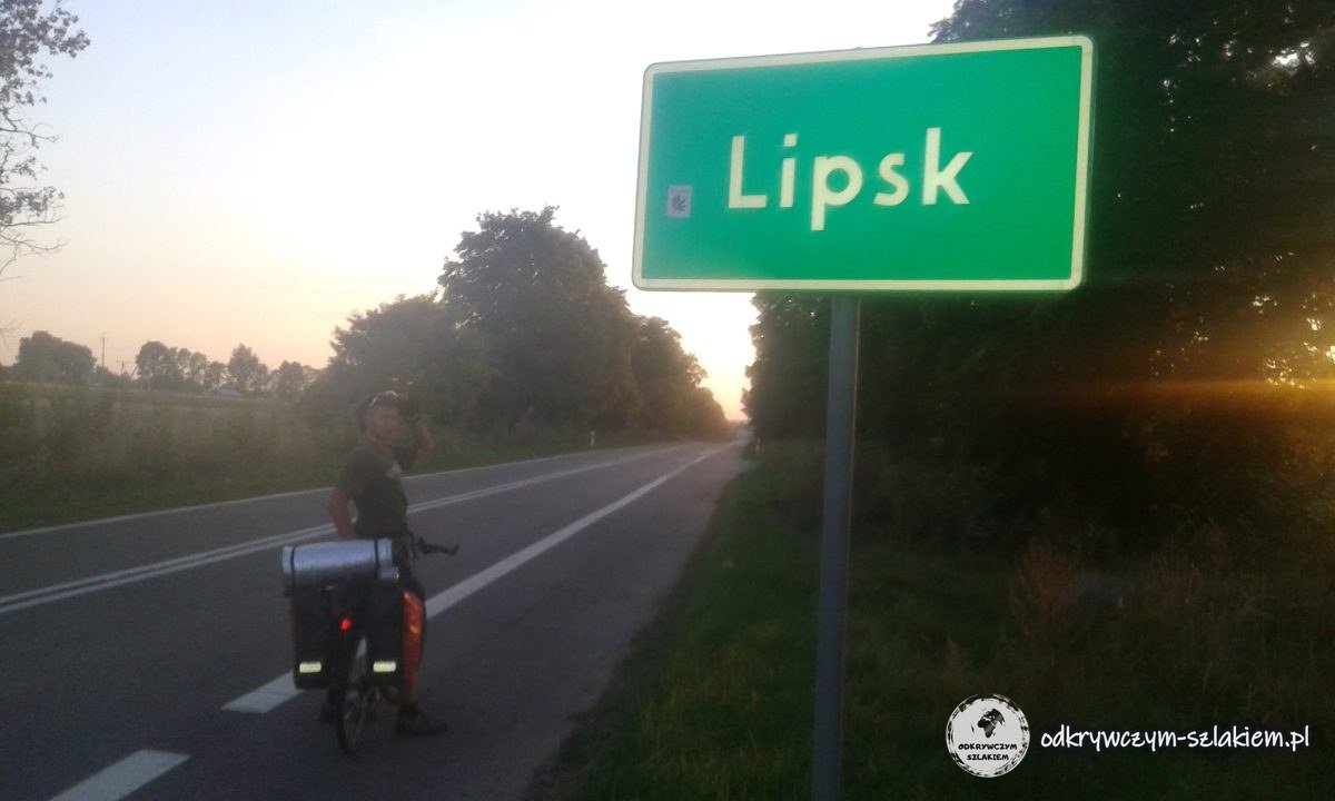 Michał mit seinem Rad am Ortsschild von Lipsk bei Sonnenuntergang