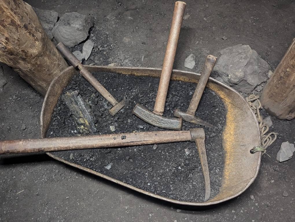Stare narzędzia górnicze – kilof i młotki – na korycie z węglem w kopalni Guido